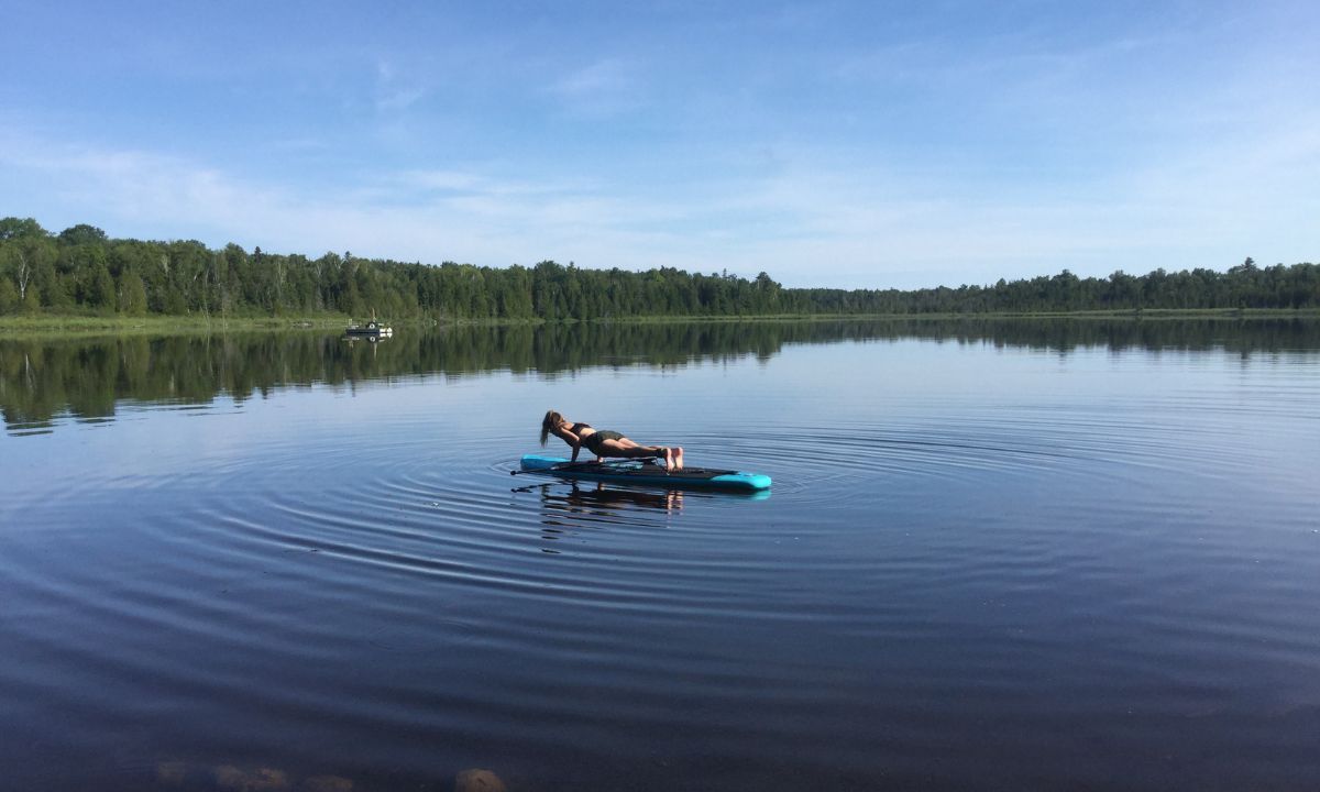 Young woman in a yoga position on her inflatable paddle board on small lake
