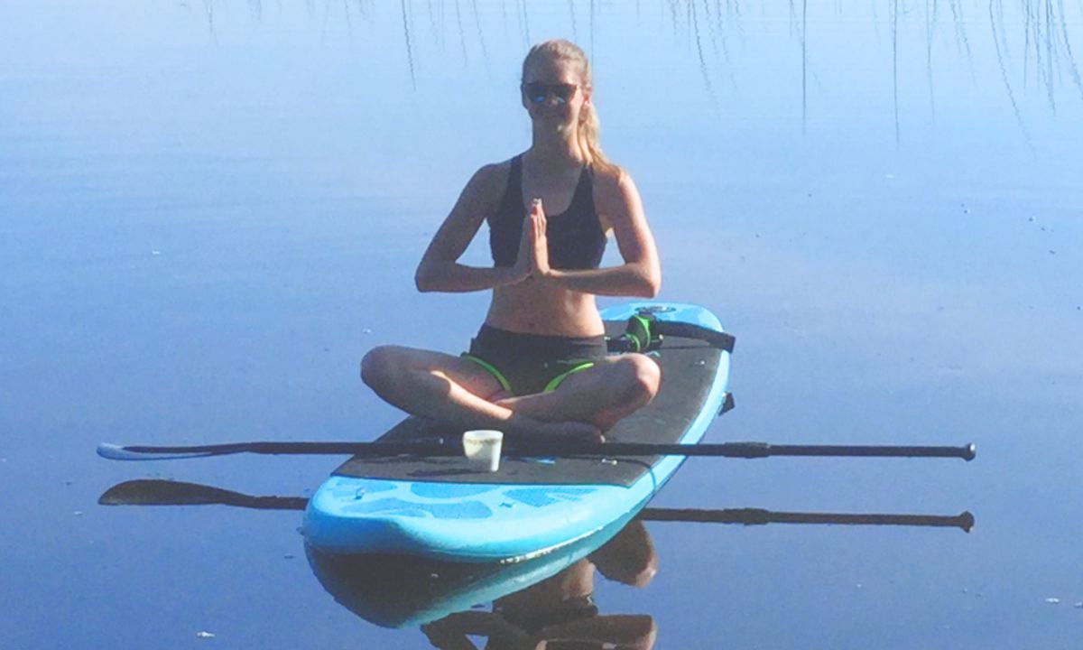 woman in yoga pose with morning coffee on an inflatable paddle board