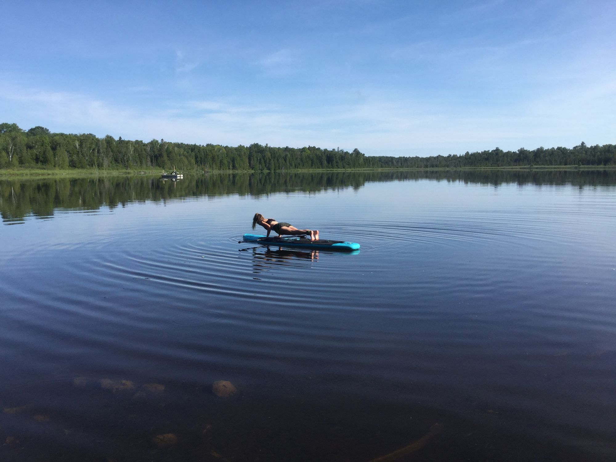 Young woman on lake doing plank Yoga Pose on Inflatable SUP board