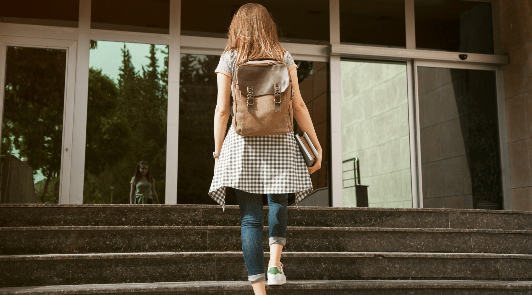 Woman entering the steps of a school with a leather backpack