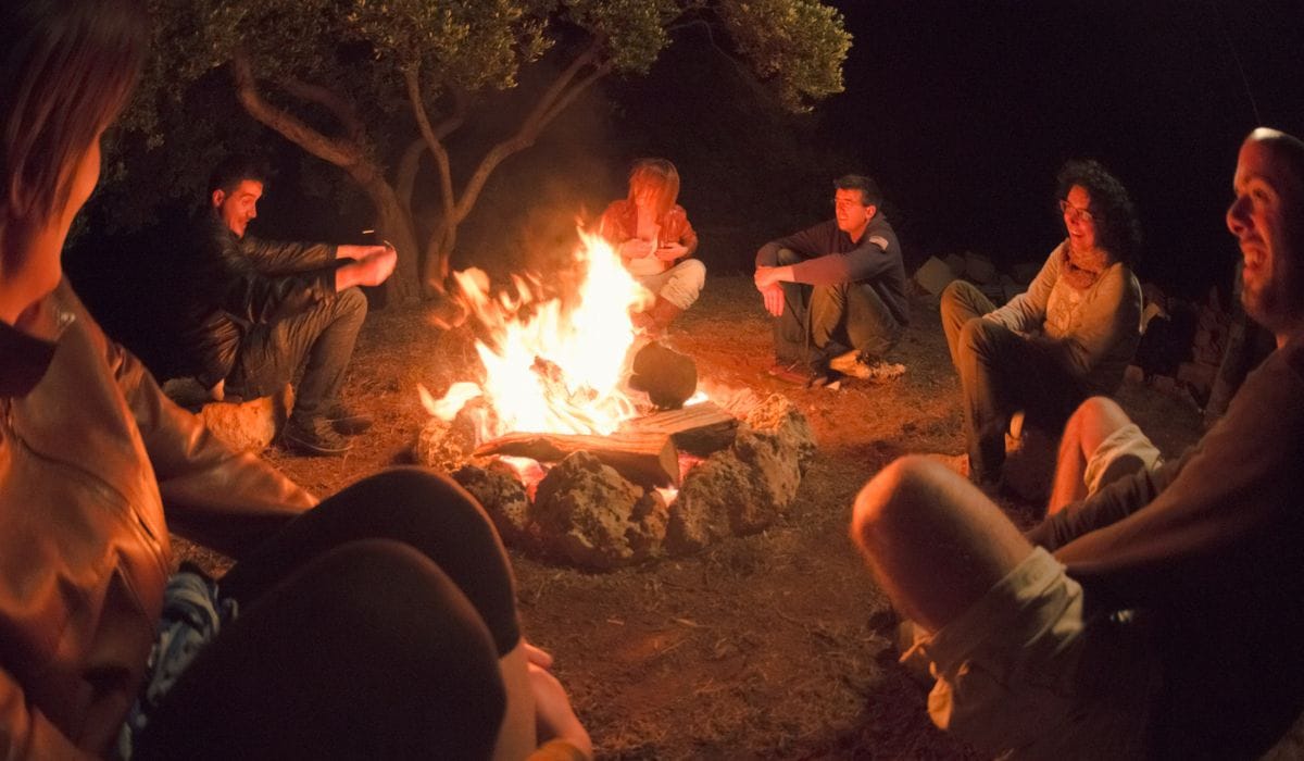 Group of friends sitting around campfire at night