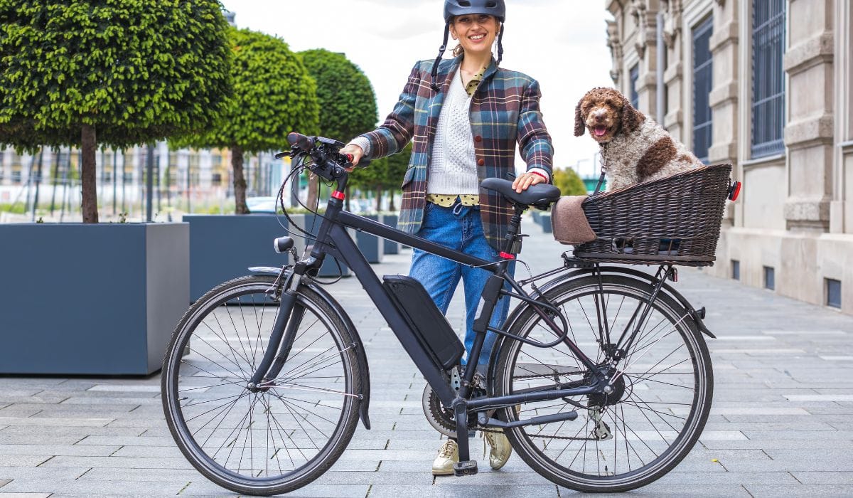 A woman wearing bike helmet with her commuter ebike and dog in basket at the back